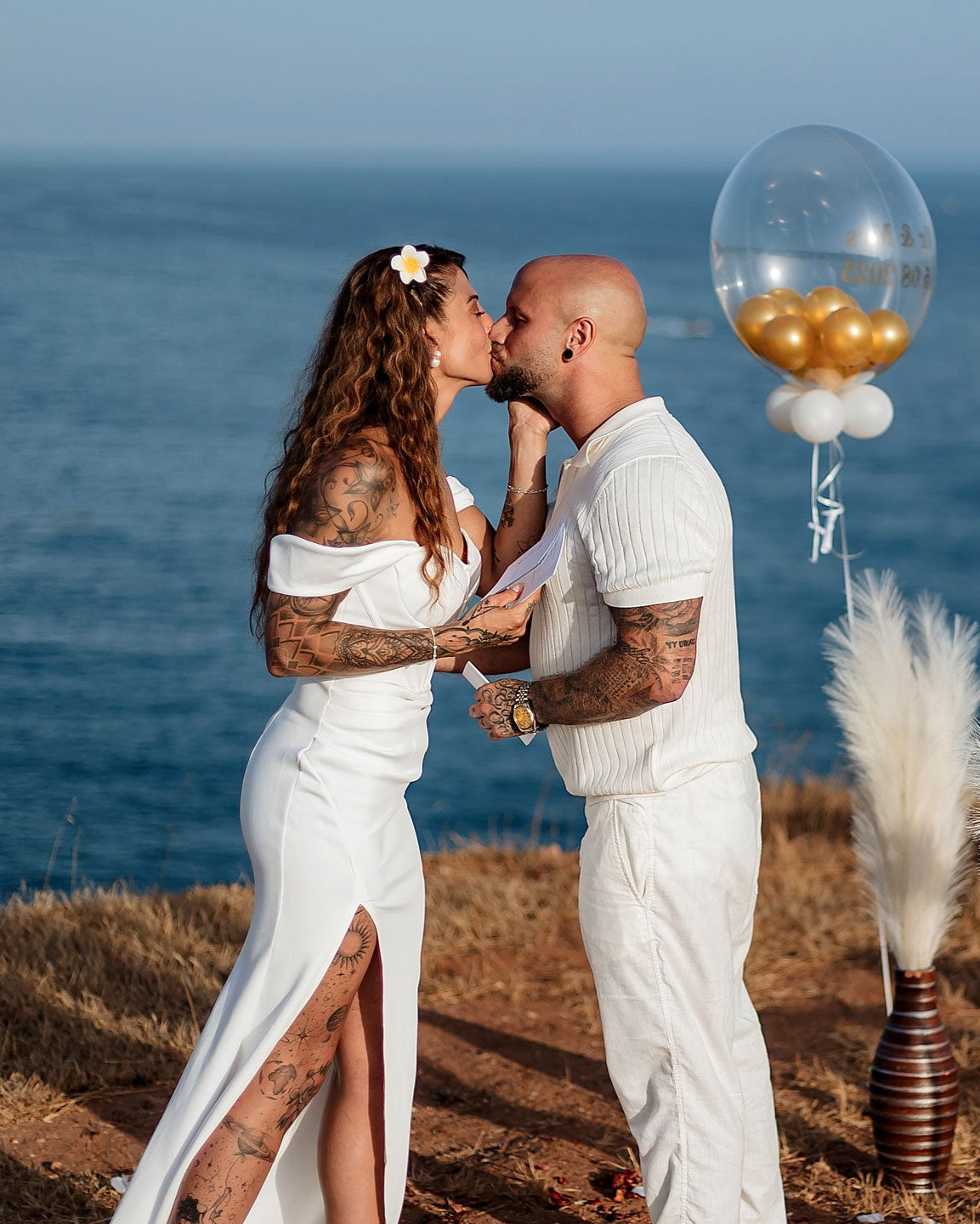 Brautpaar bei freier Trauung am Klippenrand der Algarve, Boho-Dekoration mit Pampasgras und Blick aufs Meer.