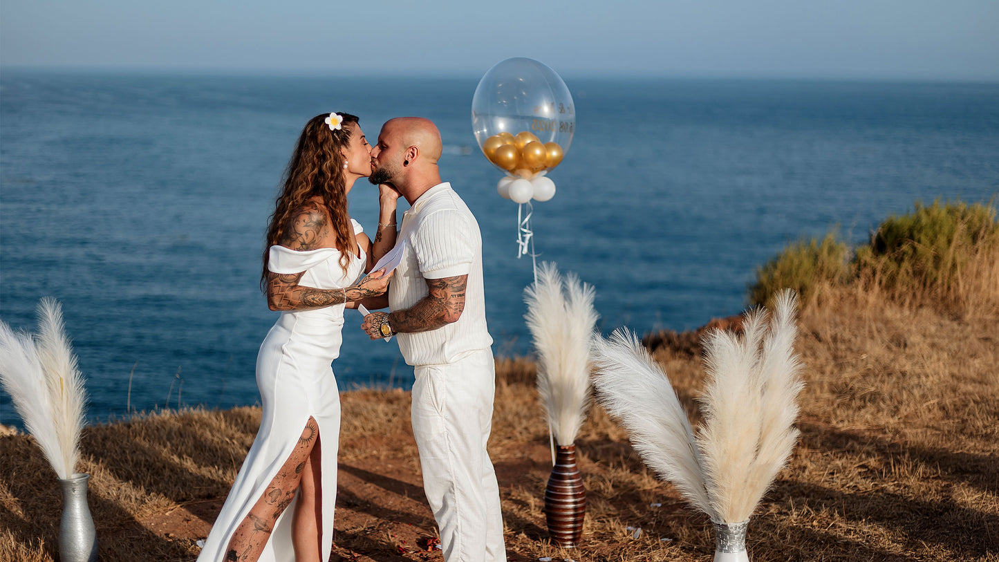 Brautpaar bei freier Trauung am Klippenrand der Algarve, Boho-Dekoration mit Pampasgras und Blick aufs Meer.